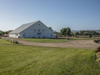 a white barn on a grassy lot with a bike and grass trail near it in the foreground