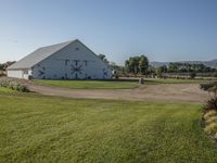 a white barn on a grassy lot with a bike and grass trail near it in the foreground