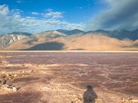 a man is standing at the edge of a red desert with mountains in the background