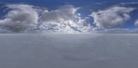 the snow covered ground is under an intense sky with fluffy white clouds above it and a yellow and blue umbrella on one side