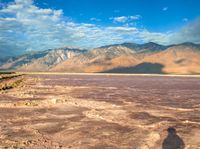 shadow of a person standing on the ground in front of mountains and water filled desert