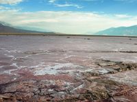 a lake filled with pink colored water under a cloudy sky near mountains at the top