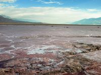 a lake filled with pink colored water under a cloudy sky near mountains at the top