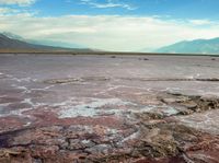 a lake filled with pink colored water under a cloudy sky near mountains at the top