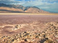 the desert has pink rocks and brown, cracked muds, while mountains are visible in the distance