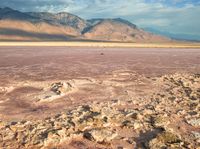 the desert has pink rocks and brown, cracked muds, while mountains are visible in the distance