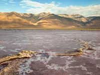 a body of water filled with lots of mud and rocks under mountains in a desert