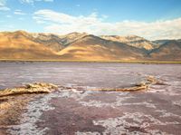 a body of water filled with lots of mud and rocks under mountains in a desert