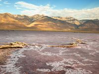 a body of water filled with lots of mud and rocks under mountains in a desert