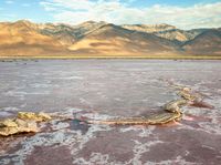 a body of water filled with lots of mud and rocks under mountains in a desert