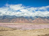 this is a mountain range with pink water on the ground and hills in the background