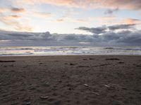 a skateboard sits on an empty beach near the ocean at sunset with dark clouds