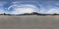 a wide panoramic view of the sand dunes, some trees and clouds in the sky