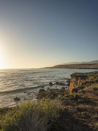 a grassy field by the shore and a cliff with rocks in the ocean in the background