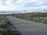 a lone road that runs near the beach next to the ocean shore on an overcast day