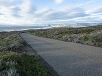 a lone road that runs near the beach next to the ocean shore on an overcast day