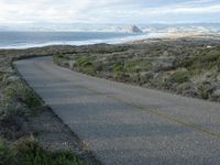 a lone road that runs near the beach next to the ocean shore on an overcast day