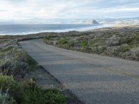 a lone road that runs near the beach next to the ocean shore on an overcast day