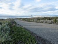 a lone road that runs near the beach next to the ocean shore on an overcast day