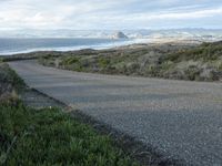 a lone road that runs near the beach next to the ocean shore on an overcast day