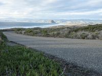 a lone road that runs near the beach next to the ocean shore on an overcast day