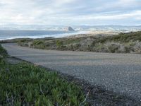 a lone road that runs near the beach next to the ocean shore on an overcast day