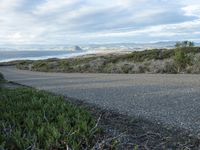 a lone road that runs near the beach next to the ocean shore on an overcast day