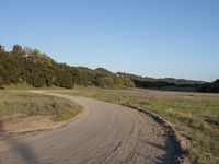 a dirt road in front of a lush green hillside side forest with a clear blue sky