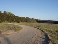 a dirt road in front of a lush green hillside side forest with a clear blue sky