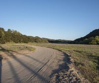 a dirt road in front of a lush green hillside side forest with a clear blue sky