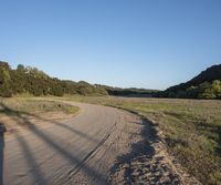 a dirt road in front of a lush green hillside side forest with a clear blue sky