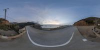 a fish - eye view of a scenic road with cars and a bicycle rider in the middle