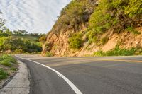 the road is empty but winding down the mountain side the side has a hillside on it and a treeline in front