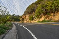 the road is empty but winding down the mountain side the side has a hillside on it and a treeline in front