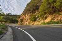 the road is empty but winding down the mountain side the side has a hillside on it and a treeline in front