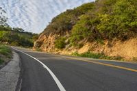 the road is empty but winding down the mountain side the side has a hillside on it and a treeline in front