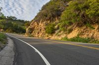 the road is empty but winding down the mountain side the side has a hillside on it and a treeline in front