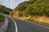 the road is empty but winding down the mountain side the side has a hillside on it and a treeline in front