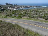 a person riding a skate board on a scenic road near the ocean during the day