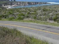 a person riding a skate board on a scenic road near the ocean during the day