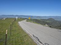 a roadway on the side of a hill with mountains in the background, and a road sign above it