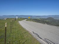 a roadway on the side of a hill with mountains in the background, and a road sign above it