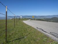 a roadway on the side of a hill with mountains in the background, and a road sign above it