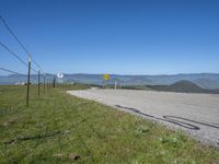 a roadway on the side of a hill with mountains in the background, and a road sign above it