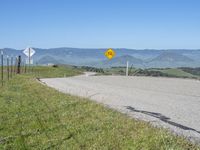 a roadway on the side of a hill with mountains in the background, and a road sign above it