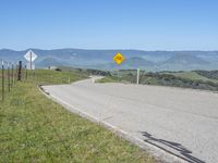 a roadway on the side of a hill with mountains in the background, and a road sign above it