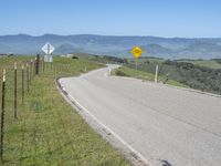 a roadway on the side of a hill with mountains in the background, and a road sign above it