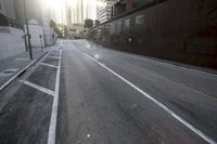 empty street near city buildings and fenced in area with sun glaring behind wall and shadows from street lights