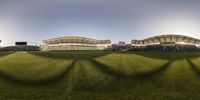 green grass with a fence and large stands in the background and an empty baseball field