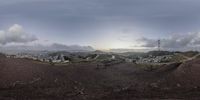 a panoramic photo showing some dirt hill with clouds over the mountains and town